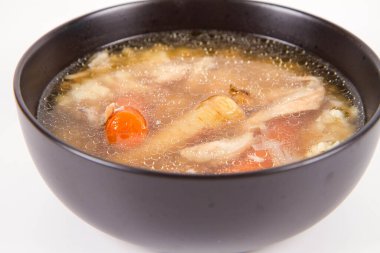 Chicken soup with noodle and carrot and parsley roots, chicken meat visible, in a bowl on a white background