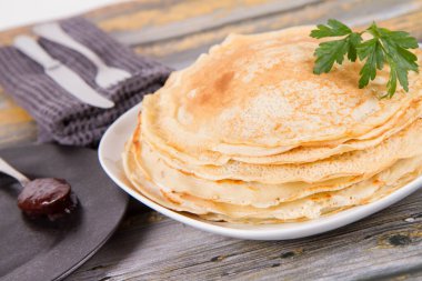 Pile of crepes with some plum jam on the side decorated with parsley leaf