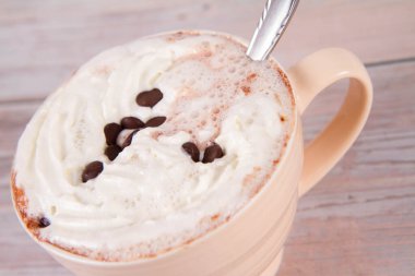 Cup of hot chocolate with whipped cream sprinkled with chocolate chips on a wooden background