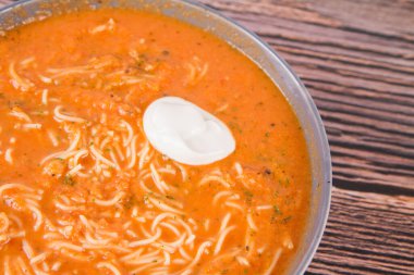 Erişteli domates çorbası ve ahşap arka planda bir kaşık krema.