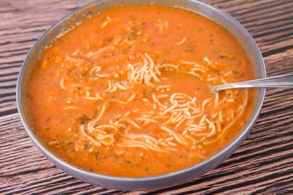 西红柿汤和面条用勺子放在木制背景上吃 — 图库照片