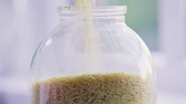 Pirinç yavaşça cam kavanoza dökülüyor. Yiyecek depolama kavramı. Yüksek kalite 4k görüntü