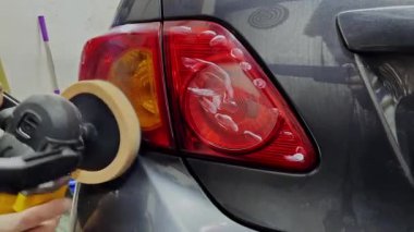 Caucasian man polishing headlights of a car using yellow polisher to clean plastic surface of lamps. High quality 4k footage