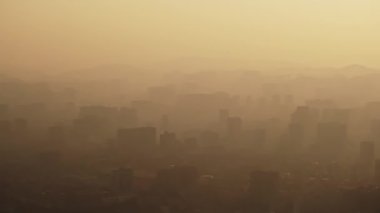 Gün batımında şehrin gökdelenlerinin ya da dağların sislerindeki dumanlı hava görüntüsü. Şehir yaşamını ve kirlilik konseptini gezin. Yüksek kalite 4k görüntü