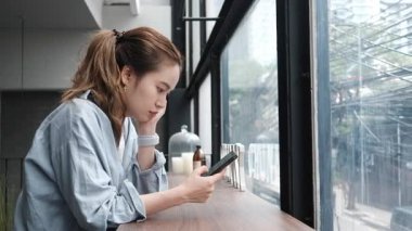 Modern Kafe 'de pencerenin yanındaki akıllı telefonu kullanan odaklanmış kadın