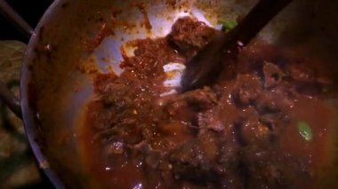 Bu yakın plan, ahşap bir kaşıkla karıştırılmış, metal bir tencerede kaynayan ev yapımı köri özünü yakalar. Zengin, karanlık sos parıldıyor, baharatların ve aromaların derinliğini ima ediyor.