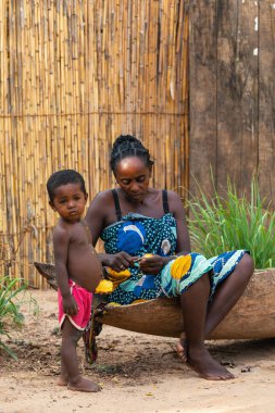 Bekopaka, Madagascar - November 5. 2022: Malagasy woman sitting on a traditional boat gives fruit to her child for breakfast.