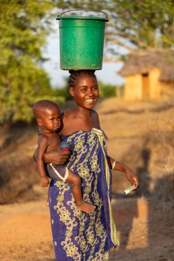 Amkilizato-Mahabo, Madagaskar - 4 Kasım 2022: Elinde bebeği ve kafasında konteynır olan kadın, Madagaskar 'ın bu kırsal kesiminde yaygın bir manzara
