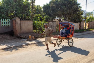 Antsirabe, Madagaskar - 2 Kasım 2022: Rickshaw koşucusu kalabalık caddelerde küçük ahşap arabasıyla koşuyor. Koşan bir kişi tarafından sürülen el arabası geleneksel ulaşım biçimidir..