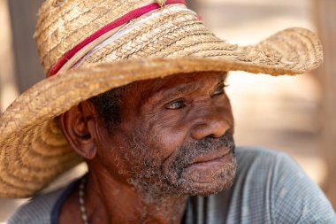 Miandrivazo, Madagaskar - 2 Kasım 2022 - Hasır şapka takan ve gülümseyen yaşlı adam. Son sınıf öğrencisi sokakta dinleniyor..
