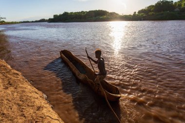 Silhouette of a Ferryman man paddling on a traditional coarse wooden boat, crossing the river Omo, Omo valley, Omorati Etiopia clipart