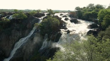 Kuzey Namibya 'daki Kunene Nehri' ndeki Epupa Şelalesi ve Güney Angola sınırı. Suyun içinde gün doğumu sisi.