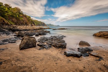 Uzun pozlama, Playa Ocotal, El Coco Costa Rica 'da kayaların üzerinde Pasifik Okyanusu dalgaları. Ünlü şnorkel plajı. Resimli cennet tropikal manzarası. Pura Vida konsepti, egzotik tropikal ülkeye seyahat.