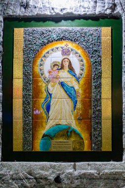 Religious artwork of the Virgin Mary displayed on the textured stone walls of the Salt Cathedral of Zipaquira, Colombia, illuminated by soft lighting in a dimly lit underground chamber. clipart