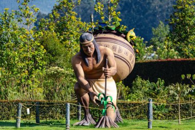 Picturesque garden path leads to Muisca tribal statue through wooden portal. Colombian heritage display in mountain eco-park setting. Ecoparque Sabana, Cundinamarca department. Colombia clipart