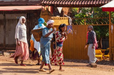 Demebecha, Ethiopia - April 20 2019: View of Ethiopian culture and daily life, featuring women walking past simple roadside structures.