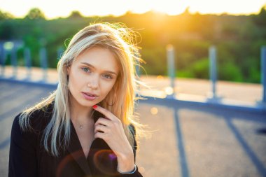 Siyah elbiseli, güzel, genç, beyaz, sarışın bir kızın yakın plan portresi. Gün batımının sıcacık ışığında duruyor. Hafifçe yeşilimsi arka planı ve fotokopi alanı var.