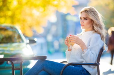 İki eliyle bir fincan kahve, büyük gümüş küpeler ve kırmızı manikür, bulanık soğuk mavimsi sonbahar arkaplanı.