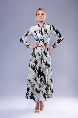 Beyaz gri arka planda benekli tasarımcı elbisesi içinde duran güzel, zayıf, beyaz, sarışın bir kızın tam boy stüdyo portresi.