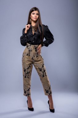 Beyaz gri bir arka planda yüksek topuklu ayakkabı giyen, kameraya poz veren ve kameraya bakan güzel, zayıf, beyaz, beyaz, esmer bir kızın tam boy stüdyo portresi.