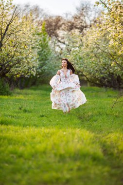Güzel esmer beyaz bir kadının portresi. Çiçekli bir elma bahçesinde beyaz çiçekli bir elbiseyle koşuyor. Yüzünden taze yeşil çimenler fırlamış, saçları uçuşuyor.