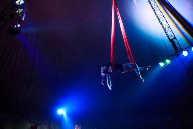 Profesyonel hava kayışları ipek kadın jimnastikçi sirk performansı Red Arena 'da arka planı koyu renkli konser ışıklarıyla aydınlatılmış, jimnastik unsuru sergiliyor.