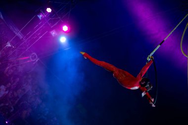 Blue Arena 'da profesyonel hava çemberi kadın jimnastikçi sirk performansı. Arka planı koyu renkli ışıklarla aydınlatılmış, jimnastik unsuru sergiliyor.