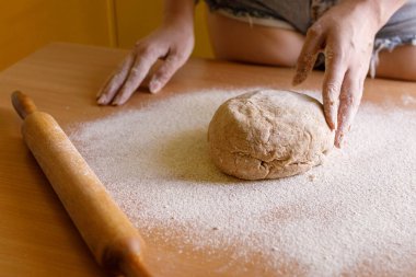 Hands working with a rolling pin on dough covered in flour. The image captures the traditional baking process on a wooden kitchen surface, highlighting a rustic home cooking experience clipart