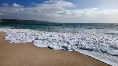 Portekiz 'de Nazare' de plaj ve dalgalar kumlu sahile yavaş çekimde yayılıyor.