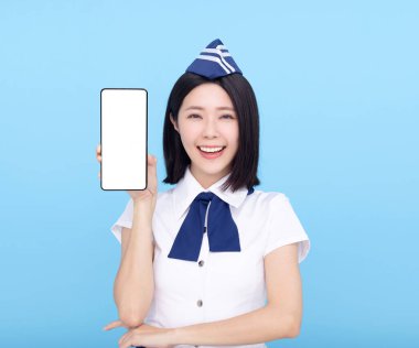 Güzel hostes cep telefonunu mavi arka planda boş ekranla gösteriyor.