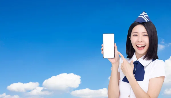 雲の背景に空白の画面で携帯電話を示す美しい航空会社のスチュワーデス — ストック写真
