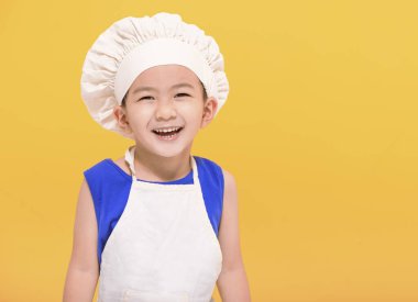 Sarı arka planda, şef üniformalı mutlu çocuk.