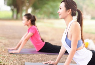 Anne ve kızı parkta çim üzerinde yoga egzersizleri yapıyor 