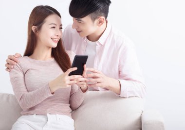 Genç çift akıllı telefon kullanıyor, internette geziniyor, internette sohbet ediyor, evdeki kanepede dinleniyor.