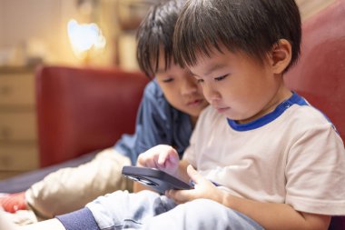 Oturma odasında cep telefonuyla online oyun oynayan mutlu çocuklar.