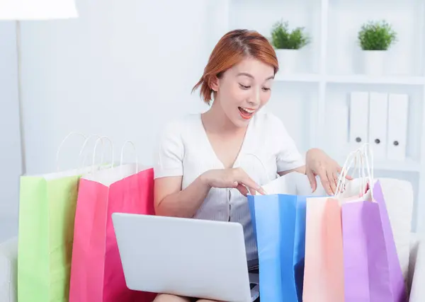 アジアの若い女性は オンラインショッピングにラップトップコンピュータを使用してショッピングバッグとソファに座っています ストック写真