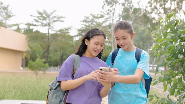 学校でスマートフォンを歩いて使用する幸せなアジアの学生の少女 ロイヤリティフリーのストック写真