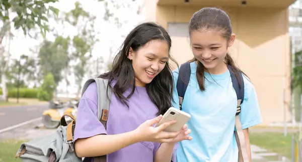 Happy Asian student girls walking and using smart phone in school