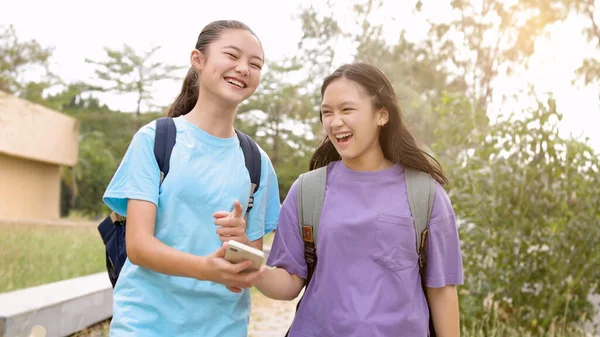 学校でスマートフォンを歩いて使用する幸せなアジアの学生の少女 ストックフォト