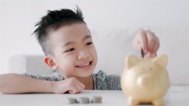 Mutlu Asyalı çocuk domuz kumbarasına bozuk para koyuyor.