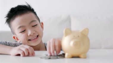 Mutlu Asyalı çocuk domuz kumbarasına bozuk para koyuyor.
