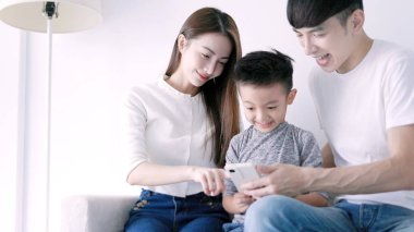 Mutlu ebeveyn ve çocuk cep telefonu kullanıyor, birlikte kanepede dinleniyorlar.