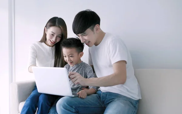 Parents with child watching funny videos using laptop browsing online tv streaming enjoying spending time together  at home in living room sitting on sofa