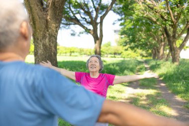 Mutlu Asyalı kıdemli çift meditasyon sırasında parkta temiz hava soluyor.