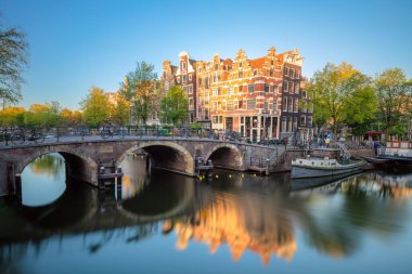 Amsterdam mı? Amsterdam 'da sabahın erken saatlerinde. Yumuşak güneş Amsterdam 'ın ünlü manzarasını aydınlatıyor. Tipik eski evler ve köprüler. Suda yansıma. Amsterdam, Hollanda, Hollanda