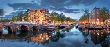 Amsterdam mı? Amsterdam 'ın tarihi şehir merkezinin panoramik manzarası. Amsterdam 'ın geleneksel evleri ve köprüleri. Mavi bir akşam ve sudaki ışıkların huzur dolu yansıması. Uzun pozlama. Tarihi bir şehre Avrupa seyahati. Avrupa, Nethe