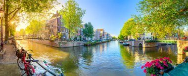Amsterdam 'ın Ruhu. Amsterdam 'da sabahın erken saatlerinde. Antik evler, köprüler, geleneksel bisikletler, kanallar, tekneler ve ağaçların arasından güneş parlıyor. Amsterdam 'ın tüm manzarasıyla panoramik manzara. Hollanda, Hollanda, Avrupa.