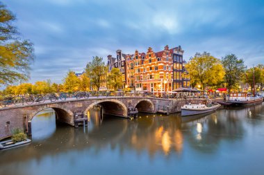 Amsterdam, Hollanda 'da sonbahar. Amsterdam 'ın tarihi şehir merkezinin panoraması. Amsterdam 'ın küçük kasabasının geleneksel evleri ve köprüleri. Romantik bir akşam ve sudaki evlerin parlak bir yansıması. Avrupa 'nın tarihi şehrine seyahat. Euro