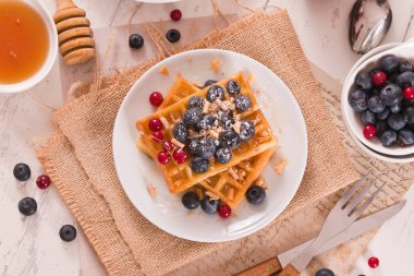 Waffles with red currant and blueberries on white dish.