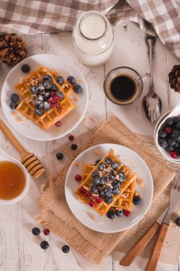 Waffles with red currant and blueberries on white dish.